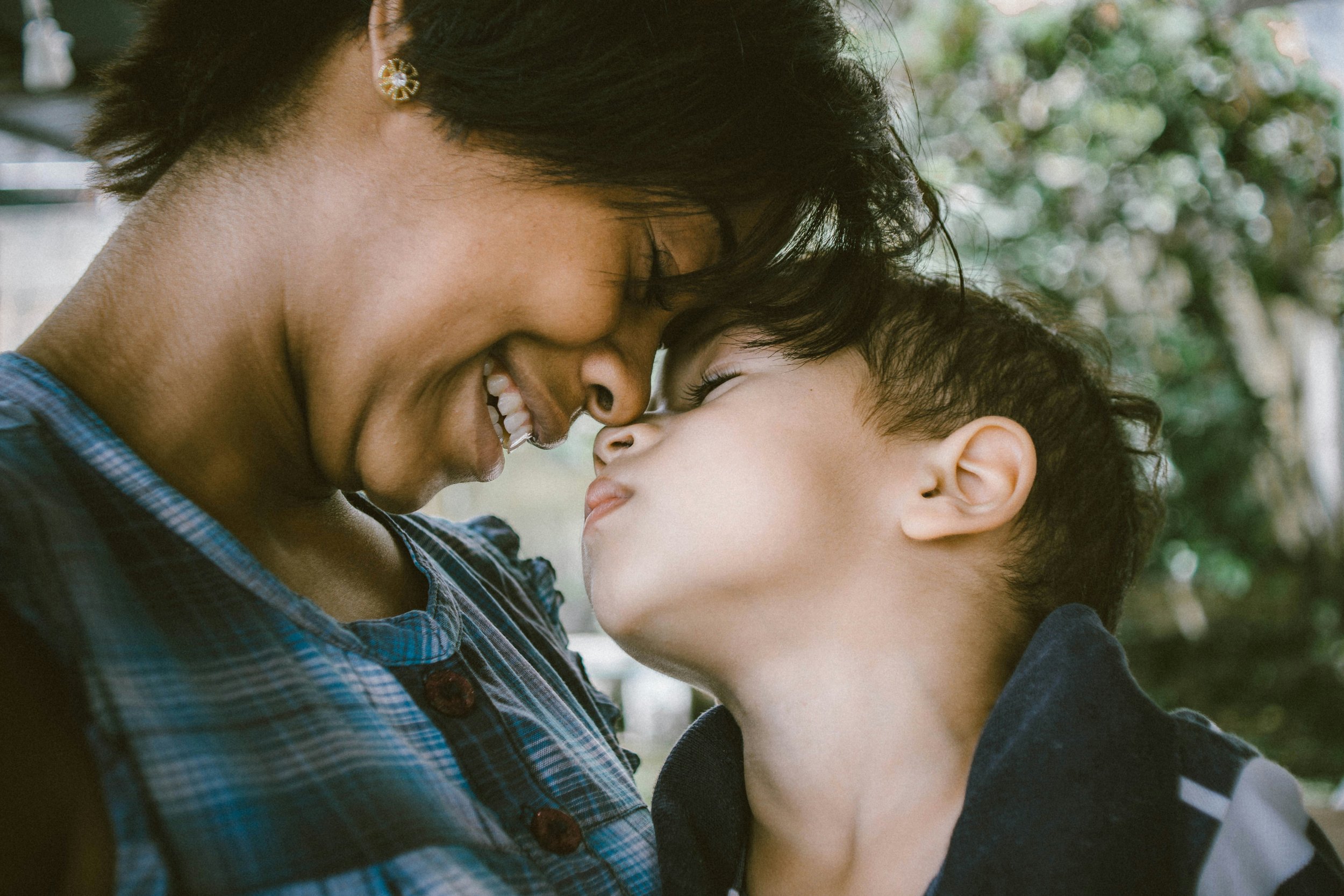 A mother and child touching noses affectionately outdoors.